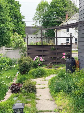 Un jardin avec un chemin de pierres, une clôture en bois et différentes espèces de plantes.