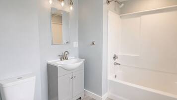 A bathroom with a toilet, sink, mirror, and bathtub.