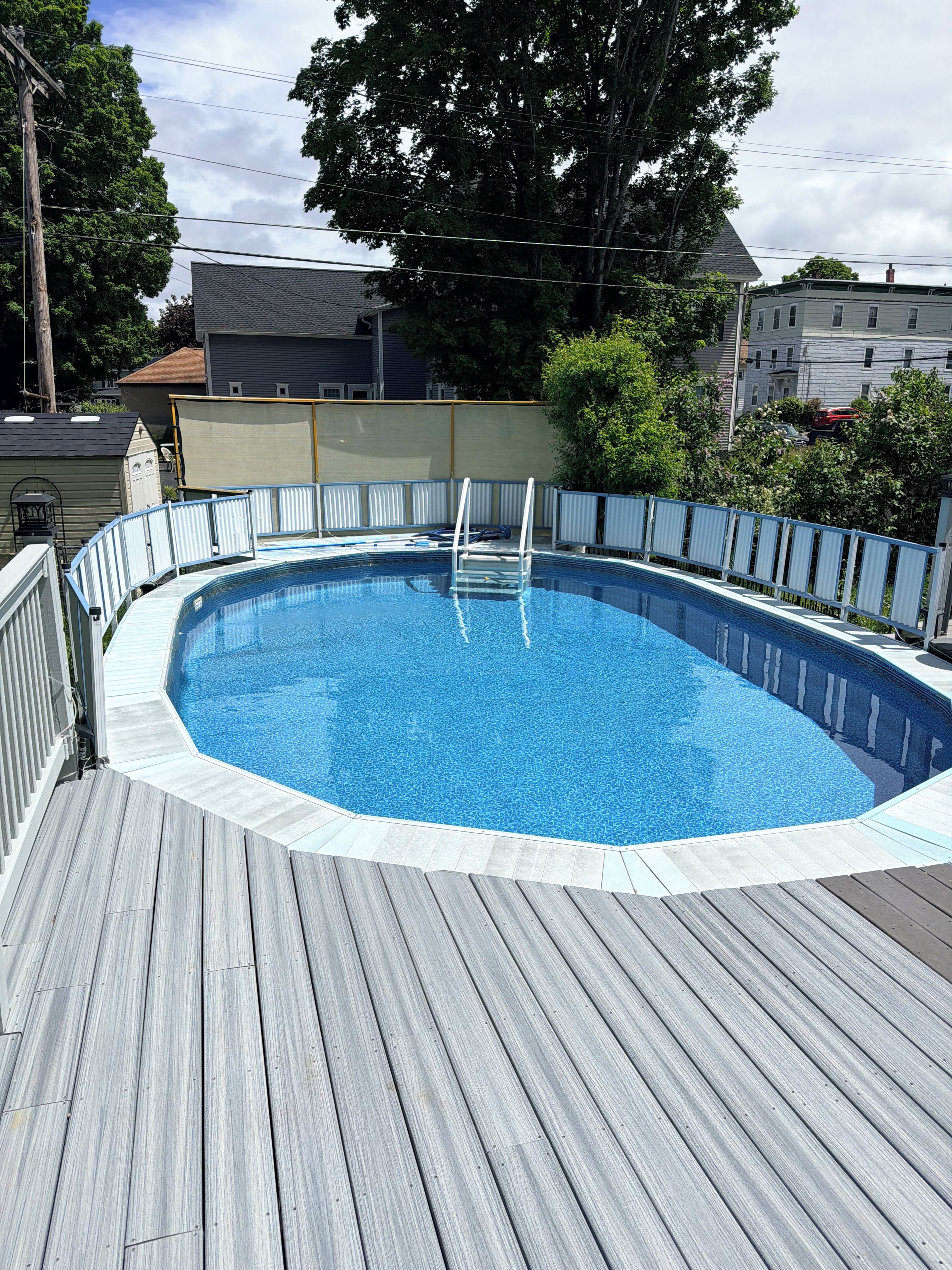 A rectangular swimming pool with a wooden deck and a metal ladder.