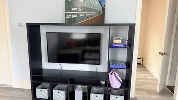 Een zwarte entertainmentkast met een flatscreen televisie, opbergmanden en een plank met een spel.