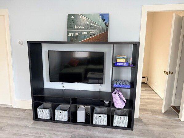 A black entertainment center with a flat-screen TV, storage bins, and a shelf with a board game.