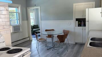A kitchen with a stove, a ceiling fan, a dining table with chairs, and a refrigerator.