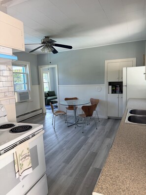 Une cuisine équipée d’une cuisinière, d’un ventilateur de plafond, d’une table à manger avec des chaises et d’un réfrigérateur.