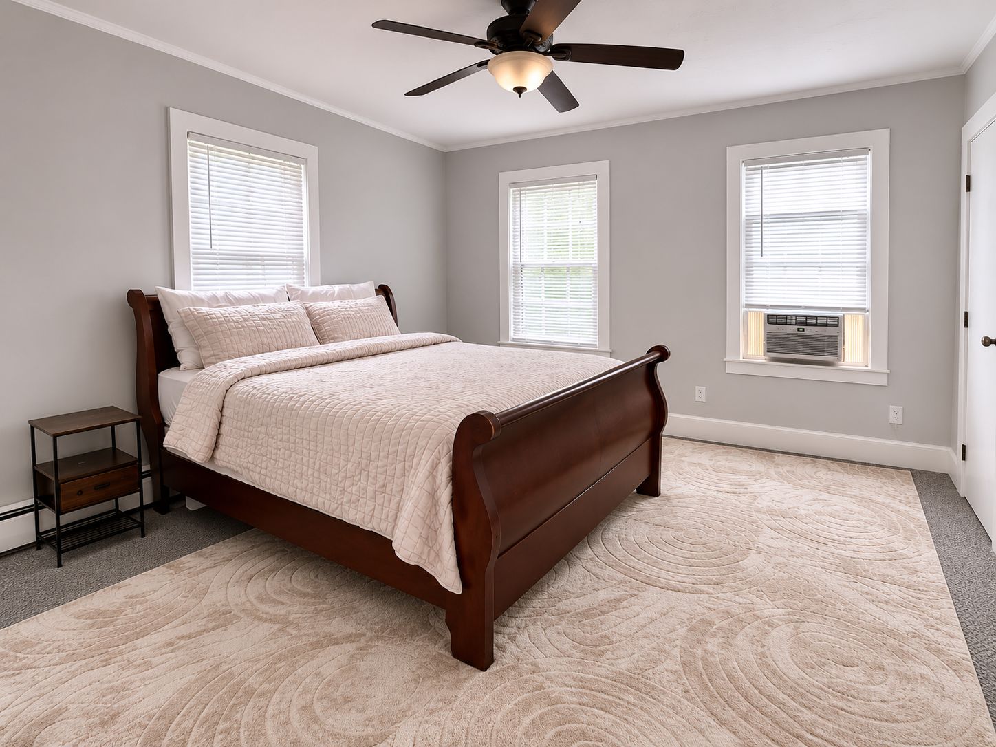 A bedroom with a bed, a nightstand, a ceiling fan, and three windows with blinds.