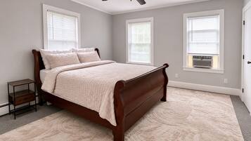 A bedroom with a bed, a nightstand, a ceiling fan, and three windows with blinds.