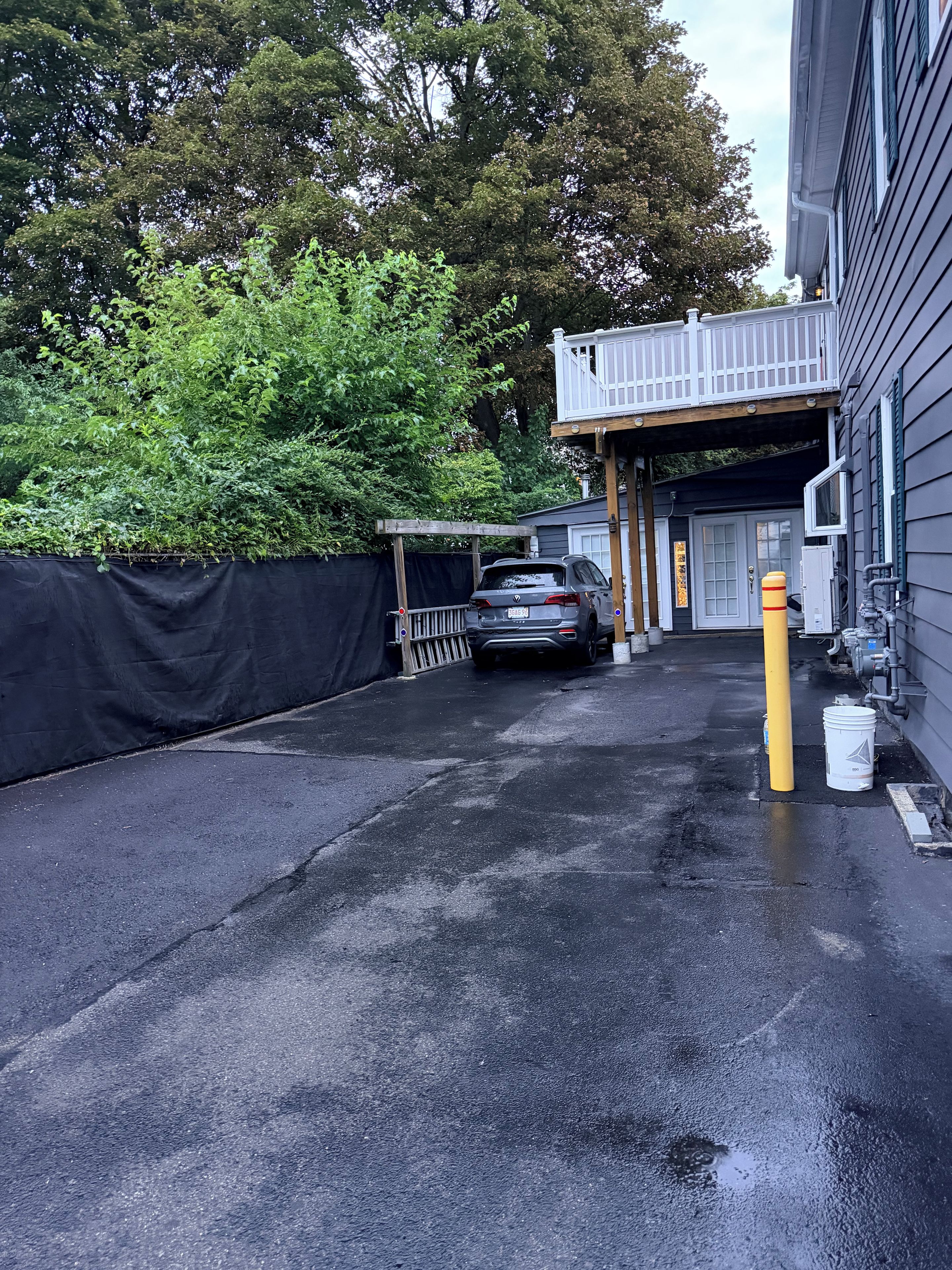 A parking area with a car, a yellow bollard, and a building with a covered entrance.