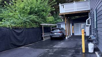A parking area with a car, a yellow bollard, and a building with a covered entrance.