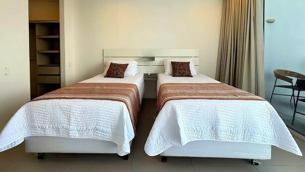 Ein Hotelzimmer mit zwei Betten, einem Kleiderschrank, einem Sessel und Blick ins Freie.