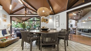 A modern dining area with a round table and wicker chairs, a hanging light fixture, and a view of the outdoors. - Vrbo Property (Açu da Torre)
