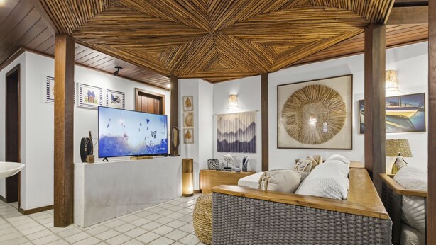 A room with a television, a sofa, a woven coffee table, and a decorative wall piece. - Vrbo Property (Açu da Torre)