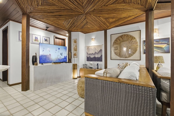 Una habitación con televisión, un sofá, una mesa de centro tejida y un adorno de pared.