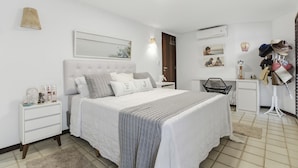 A bedroom with a bed, bedside tables, a desk, and a shoe rack. - Vrbo Property (Açu da Torre)