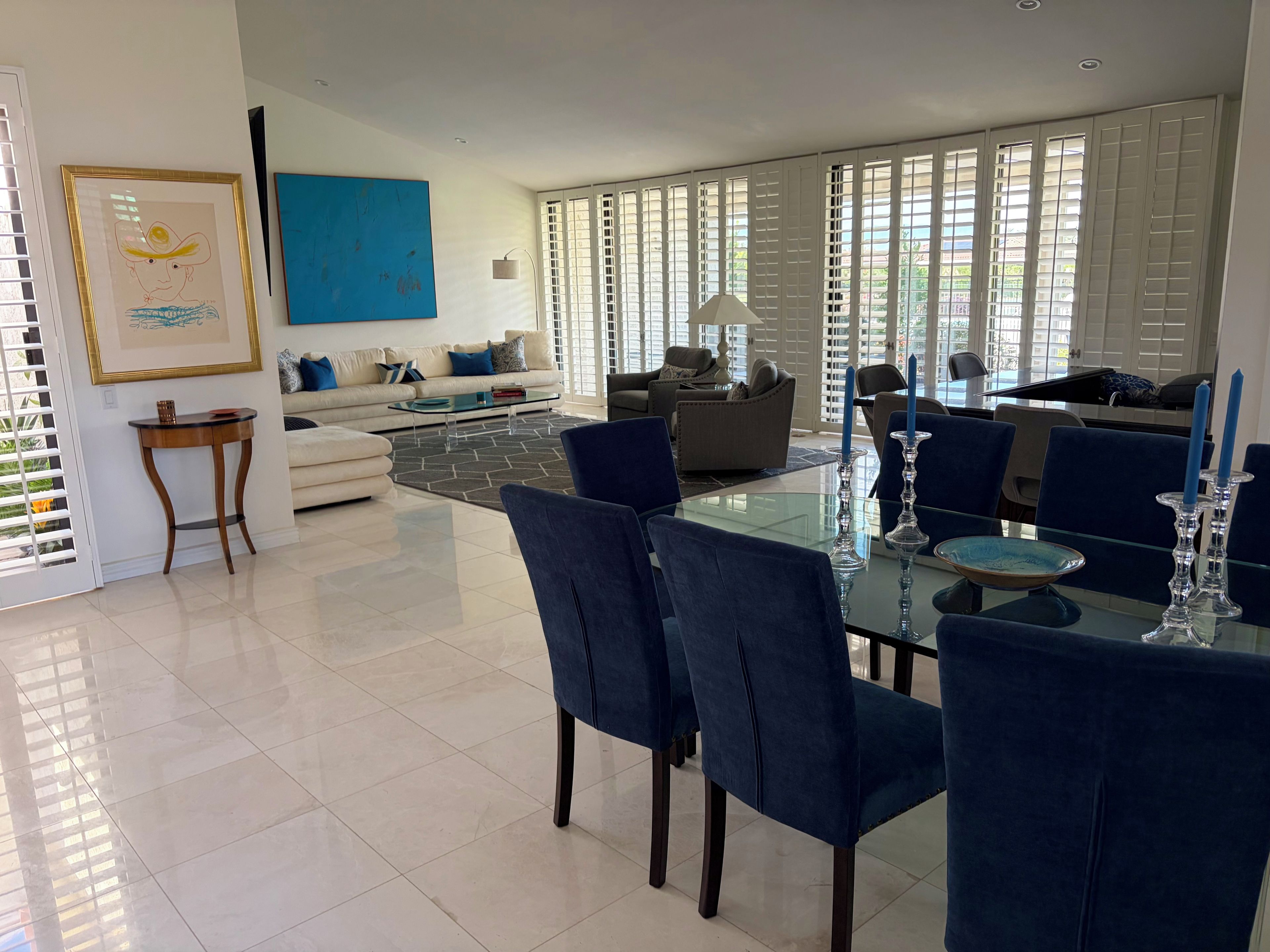 A modern living room with a glass dining table, blue chairs, and a sofa.