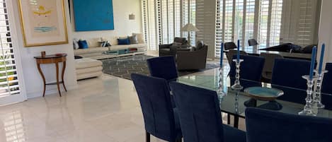 A modern living room with a glass dining table, blue chairs, and a sofa.