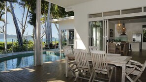 Et poolområde med træterrasse, et spisebord med stole og havudsigt.