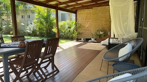 Un área de patio al aire libre con cubierta de madera, una mesa con sillas y un espacio de descanso acolchado.