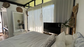 Un dormitorio con cama, televisión, espejo y ventana con cortinas.