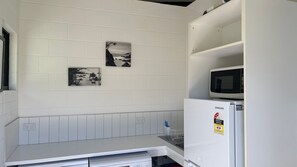A kitchen with white cabinets, a microwave, and a refrigerator. There are two black and white photographs on the wall.