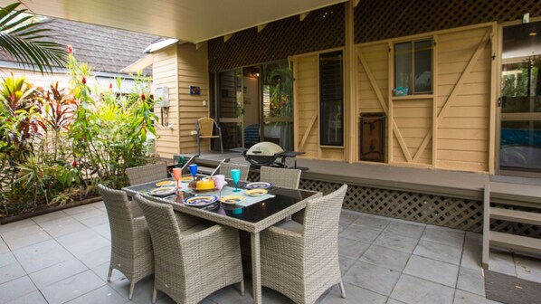 An outdoor patio with a table set for dining, surrounded by wicker chairs, and a grill in the background. - Beach Villa 4- Beachfront views (Wongaling Beach)