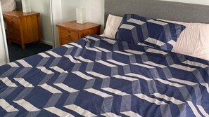 Ein Bett mit einem geometrisch gemusterten Überwurf, ein Nachttisch mit Taschentuchbox und ein Nachtschränkchen mit Schubladen.