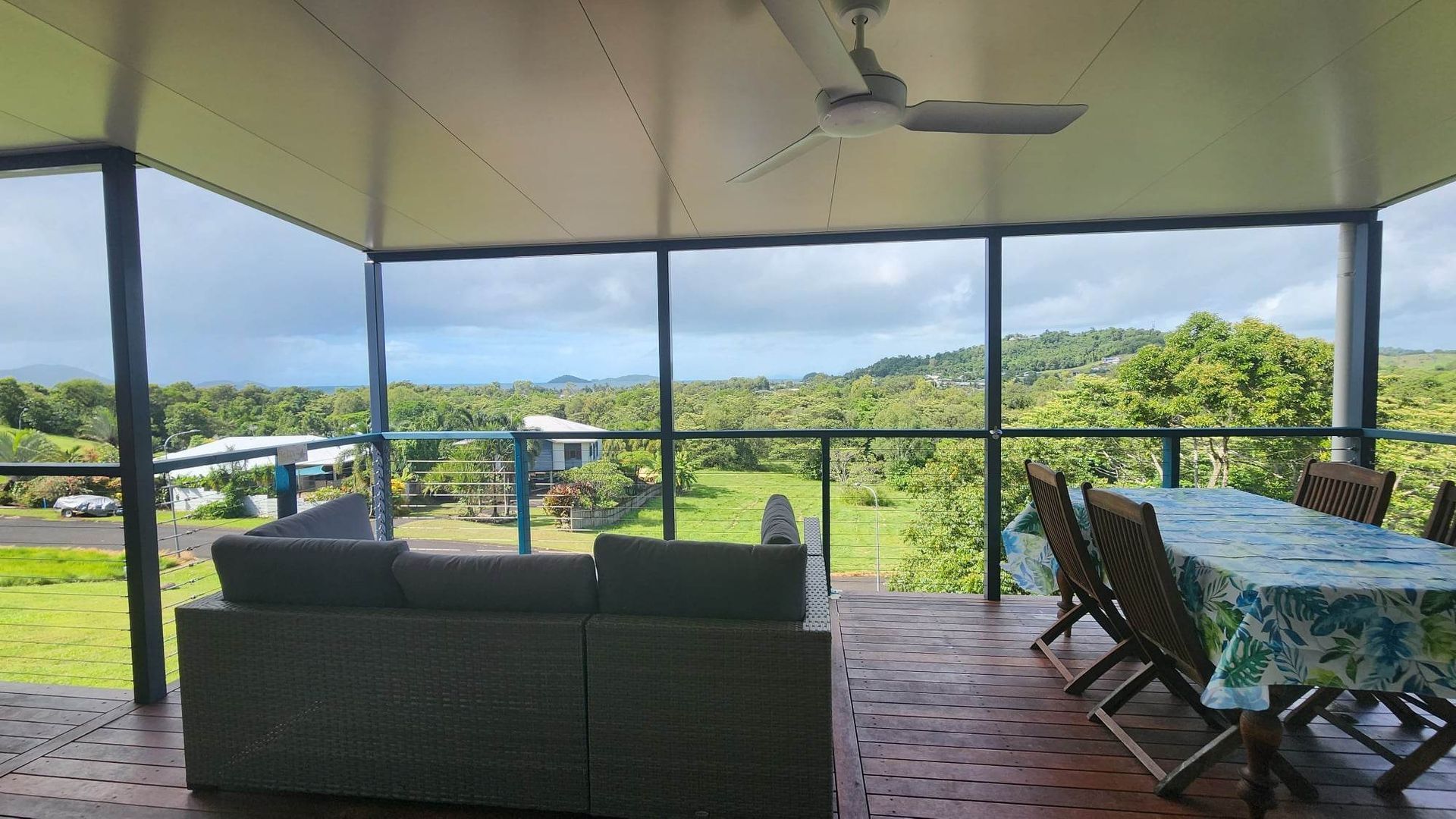 A covered outdoor area with a view of a lush landscape, a table with chairs, and a sofa.