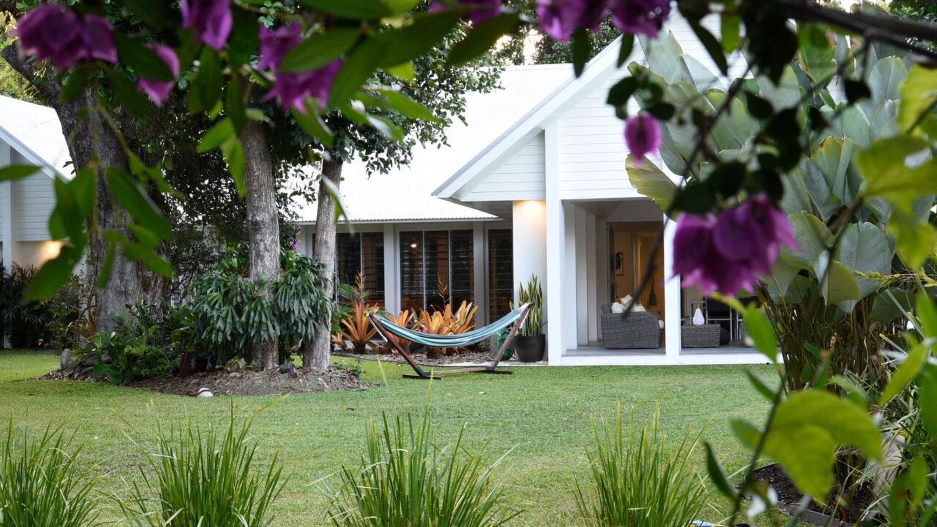 A modern house with a covered porch, a hammock, and lush greenery.