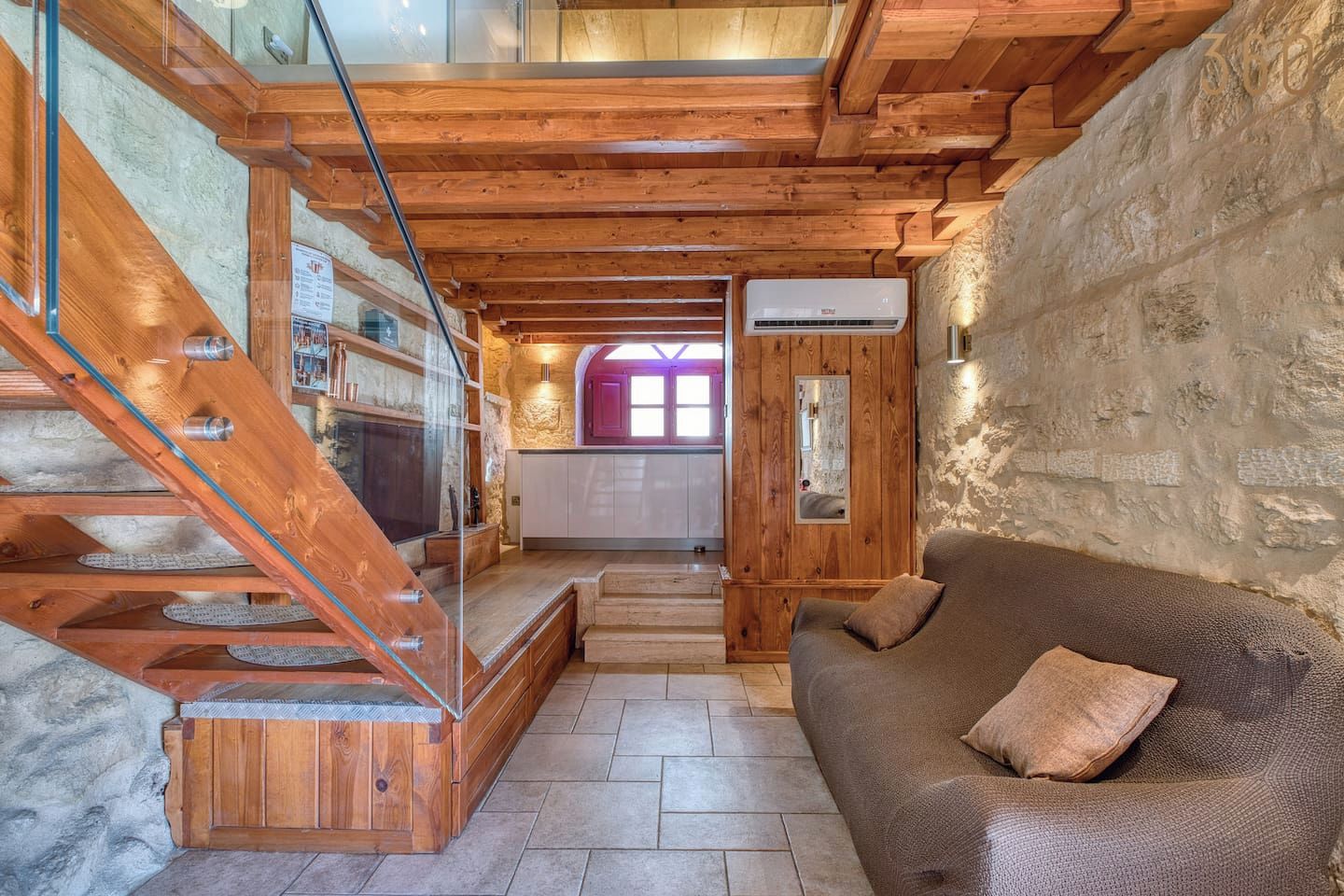 Interior em madeira com escada, sofá e área de cozinha.