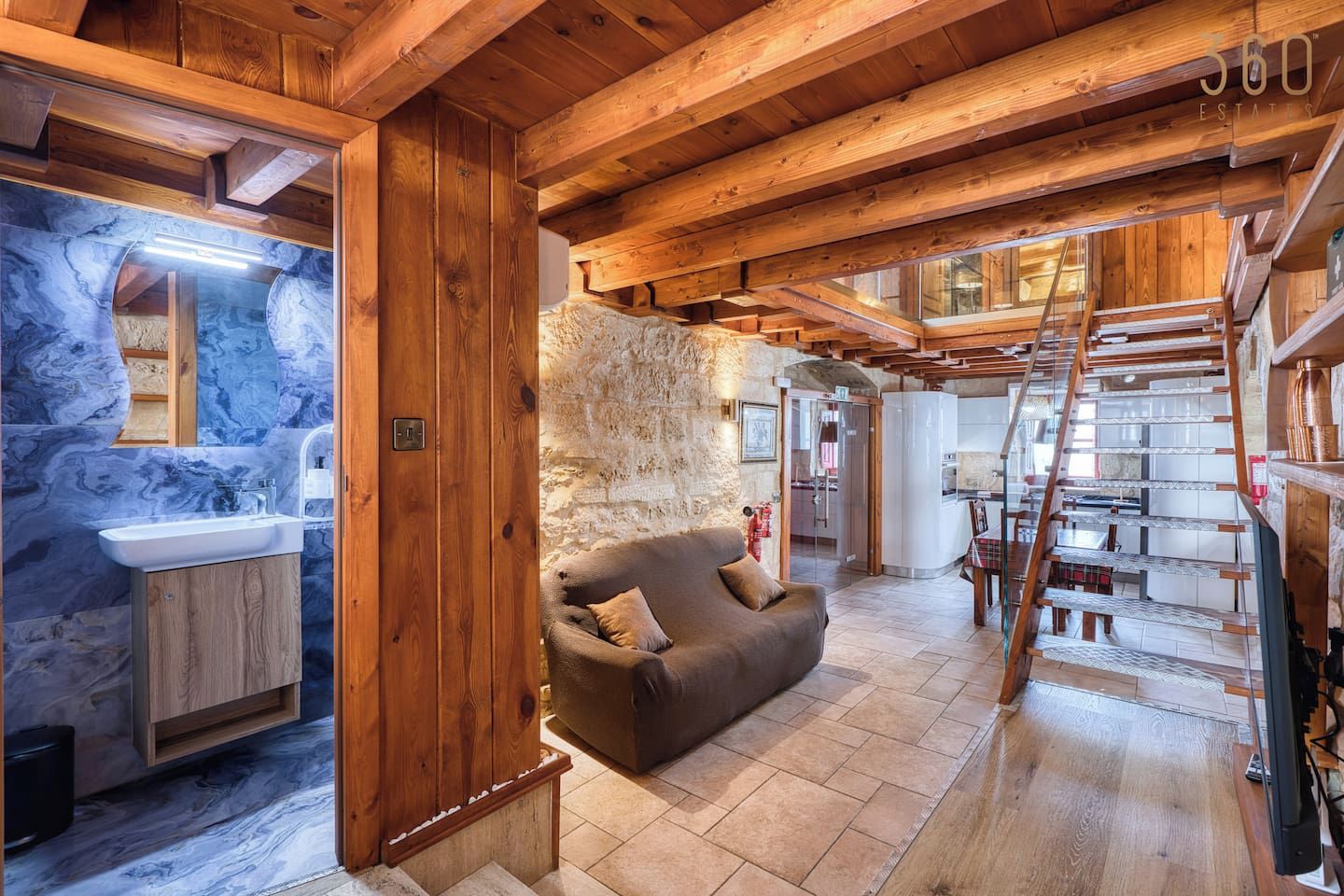 A wooden interior with a stone wall, a sofa, a sink, and a staircase.
