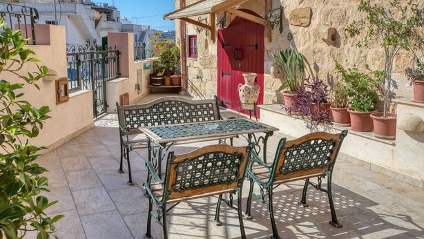 Un cortile con un tavolo e sedie, piante in vaso e una porta rossa.