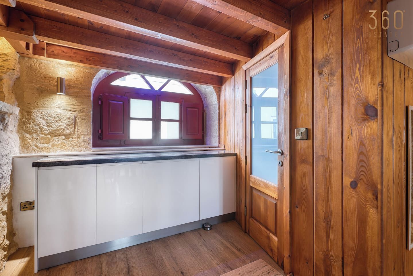A kitchen with a built-in oven, a window with a view, and wooden walls.