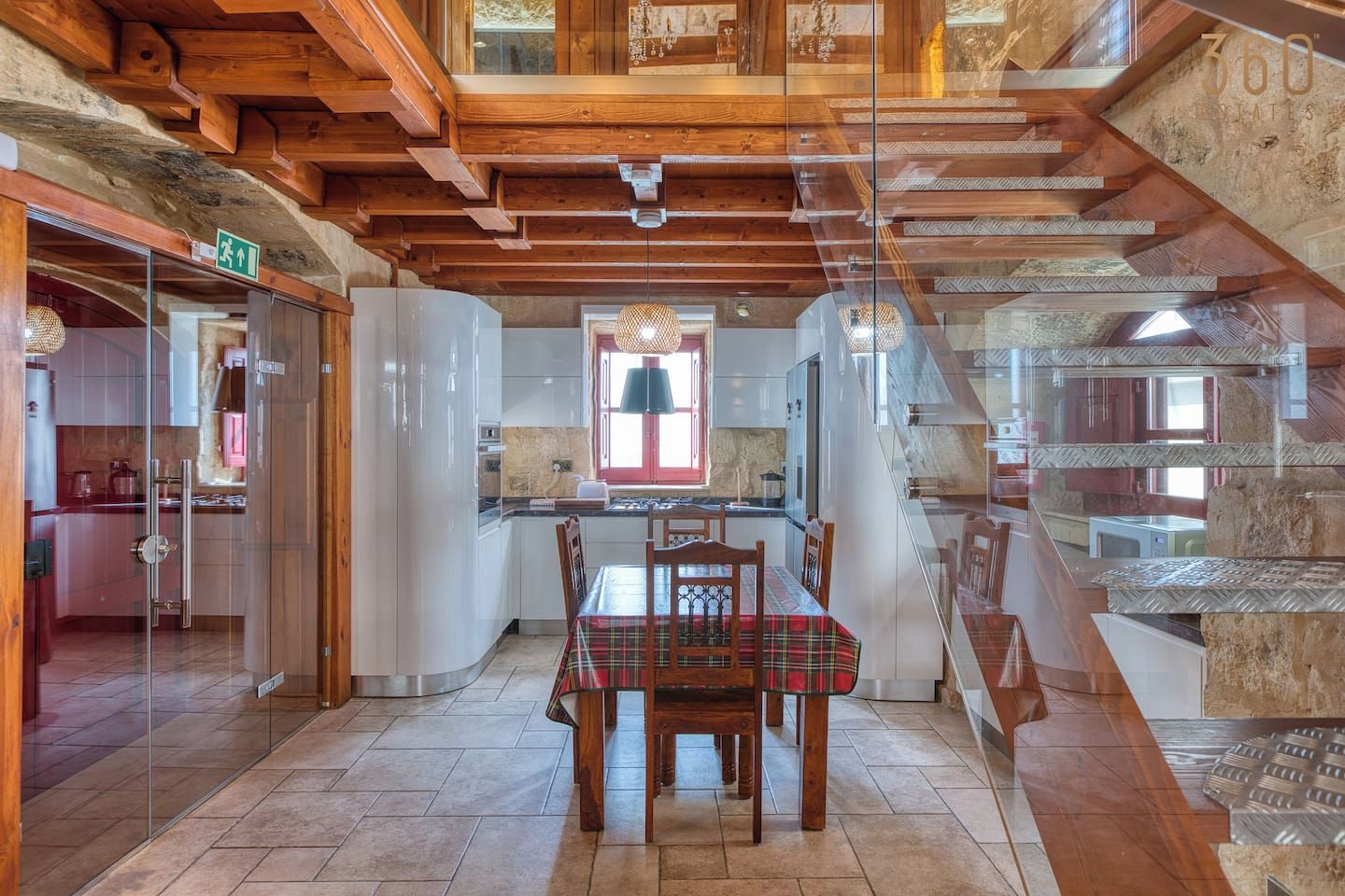 A dining area with a table and chairs, a kitchen in the background, and a staircase with a wooden interior.