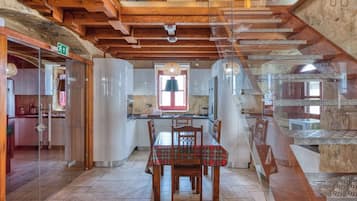 A dining area with a table and chairs, a kitchen in the background, and a staircase with a wooden interior.