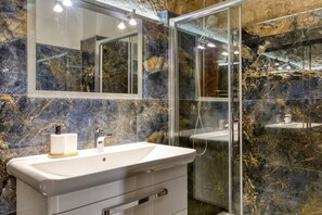 Ein Badezimmer mit Marmorwand, einer Glaskabinentrennwand und einem weißen Waschbecken mit Seifenspender.