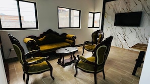 Ein Wohnzimmer mit einer Couch, zwei Sesseln, einem Couchtisch und einem an der Wand befestigten Flachbildfernseher.