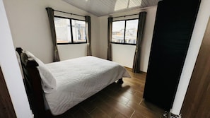 Ein Schlafzimmer mit einem Bett, zwei Fenstern und Blick auf Gebäude.