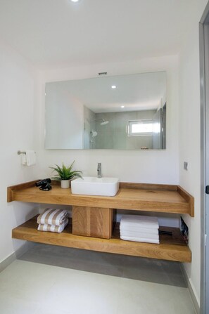 Une salle de bain moderne avec un grand miroir, un lavabo blanc et des étagères en bois.