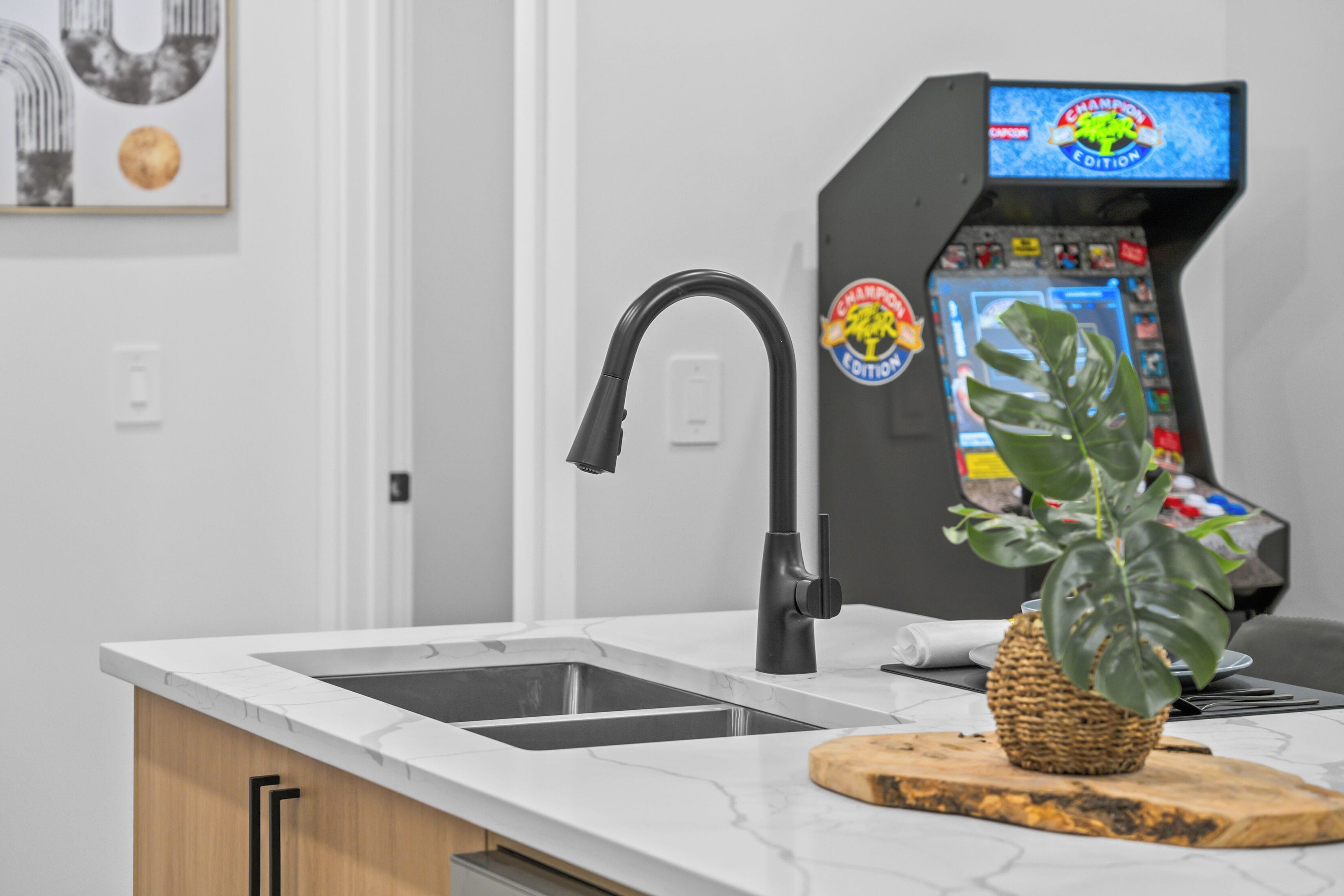 Una cocina con un grifo moderno, un lavamanos, una encimera y una máquina de juegos.