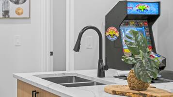 Una cocina con un grifo moderno, un lavamanos, una encimera y una máquina de juegos.