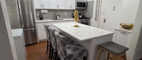 A modern kitchen with white cabinets, stainless steel appliances, a central island with bar stools, and pendant lighting.