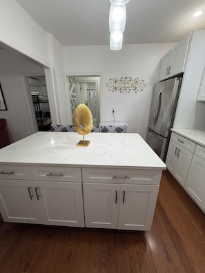 A kitchen with a large island, white cabinets, a stainless steel refrigerator, and a decorative welcome sign.