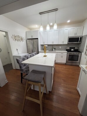 A modern kitchen with white cabinetry, a central island with bar stools, stainless steel appliances, and pendant lighting.