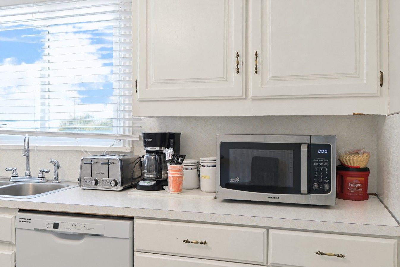 A kitchen with a toaster, coffee maker, microwave, and a red container of Folgers coffee.