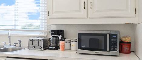 A kitchen with a toaster, coffee maker, microwave, and a red container of Folgers coffee.