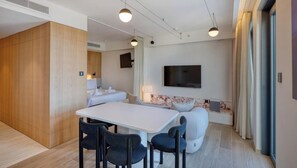 A modern hotel room with a dining area, a sofa, a TV mounted on the wall, and a large window with curtains. - One of a king Top-Floor, Jacuzzi Terrace - Mercury (St. Julian`s)