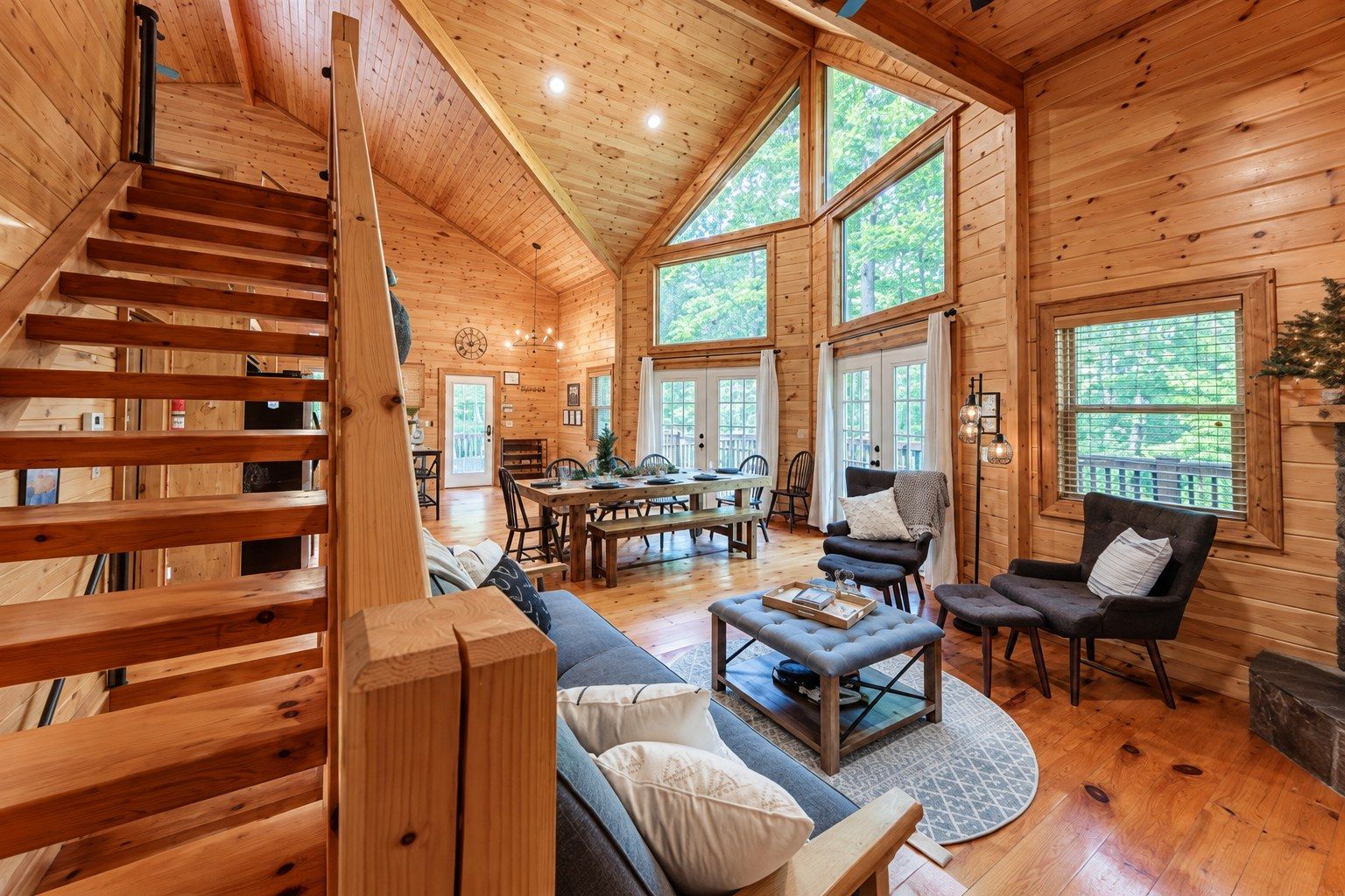 A wooden cabin interior with a staircase, dining area, and seating.