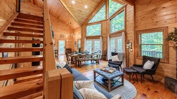 A wooden cabin interior with a staircase, dining area, and seating.