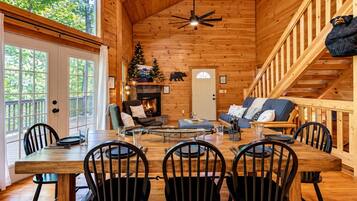 A cozy cabin interior with a dining area, a fireplace, a staircase, and a view of the outdoors.