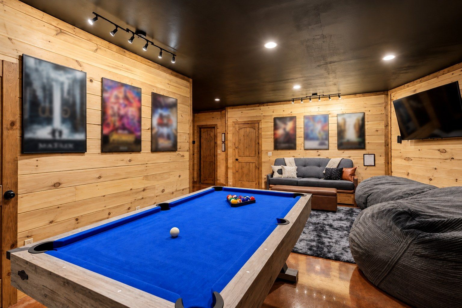A pool table in a room with wooden walls, a sofa, and a television mounted on the wall.