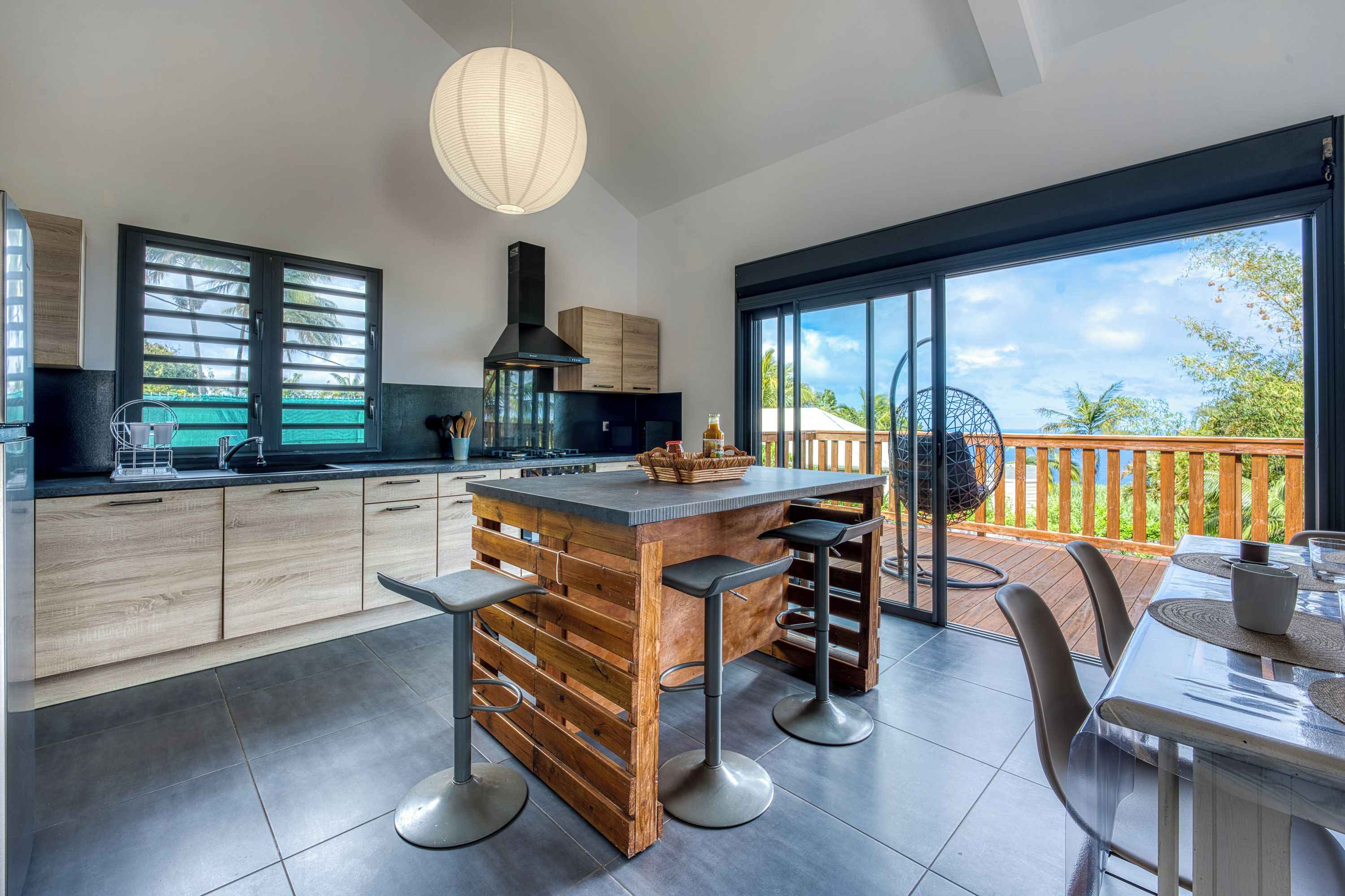 A modern kitchen with a central island, bar stools, and a large window overlooking a deck.