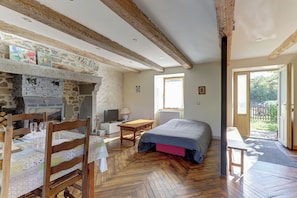Ein Zimmer mit Kamin aus Stein, Holzmöbeln, einem Bett und Blick ins Freie.